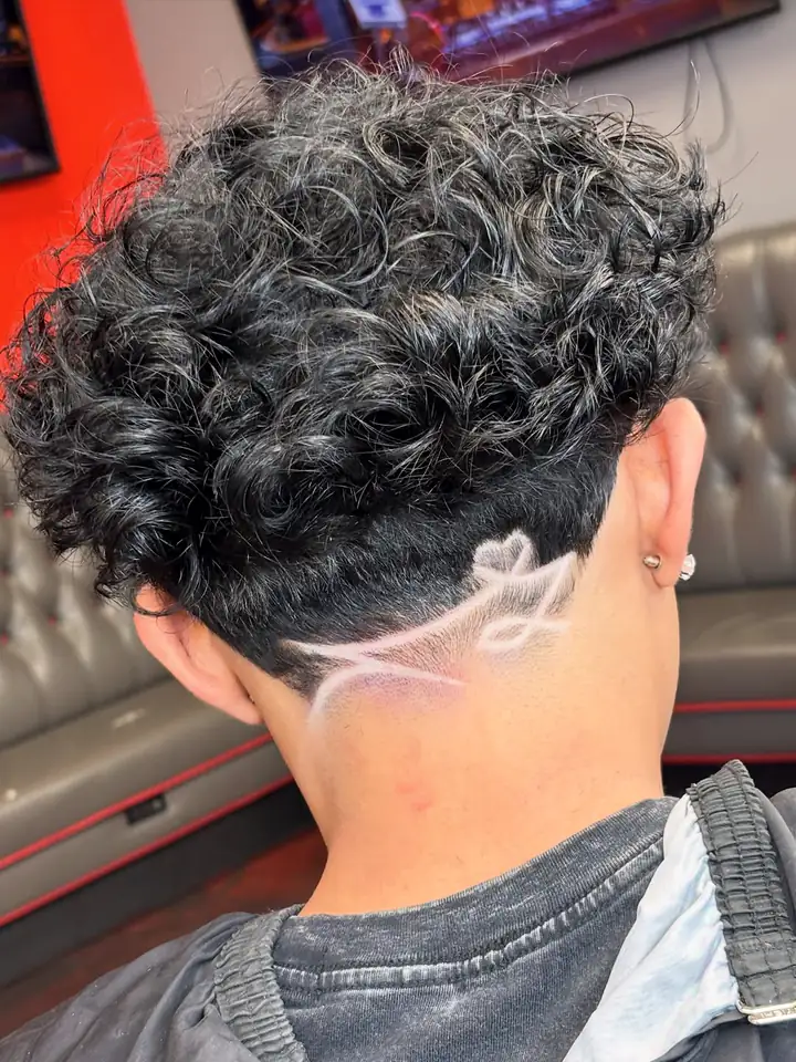 Curly top with a low taper and a freestyle design at the nape, cut by Raekwon