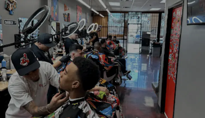 Barbers at work inside a Fresh Cuttz 2.0 shop, with ring lights over the chairs and a red sticker wall